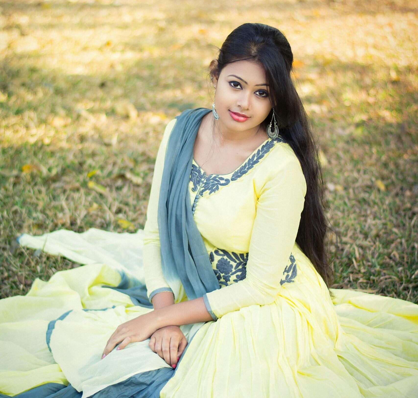 Portrait of a woman in traditional attire, sitting gracefully in a sunny park setting.