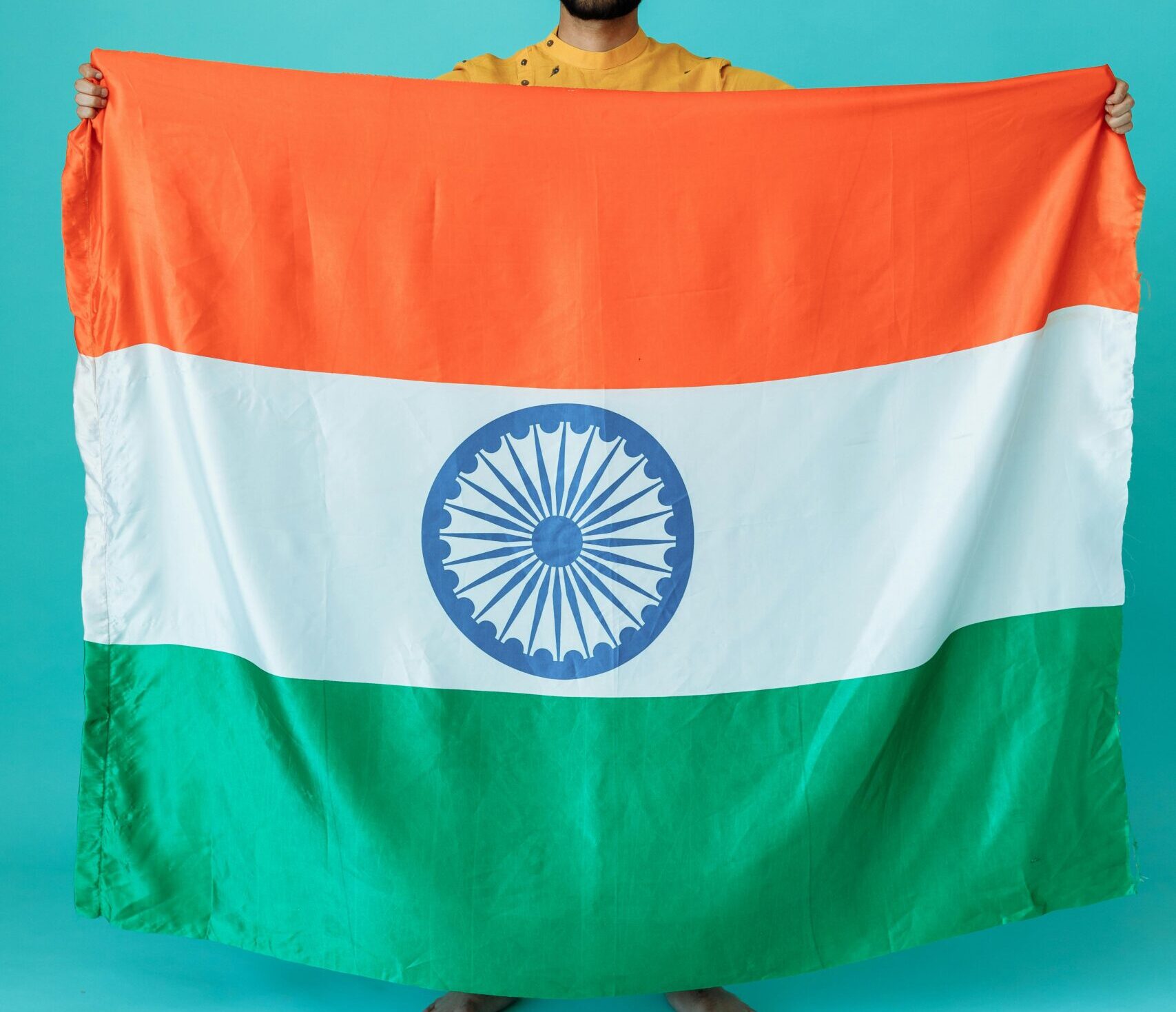 Portrait of a man holding the Indian flag against a blue background.